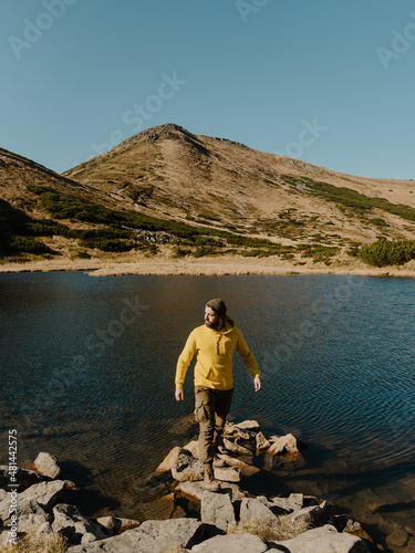 man in the yellow body shirt standing on the stone near mountain lake