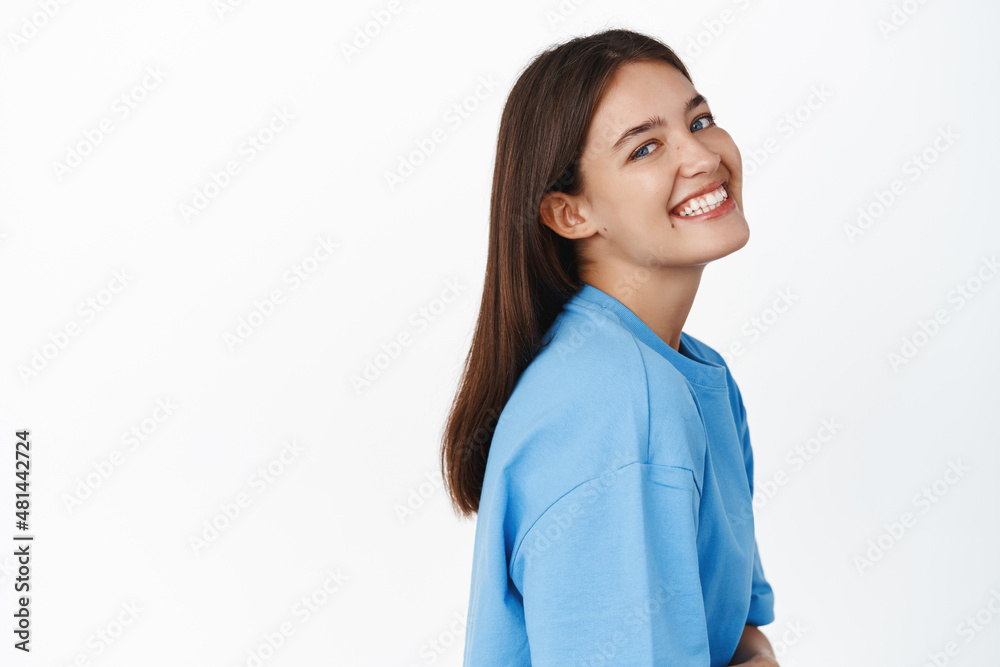 Close up portrait of smiling happy woman looking at camera in profile, wearing blue t-shirt, standing over white background Close up portrait of smiling happy woman looking at camera in profile, wearing blue t-shirt, standing over white background