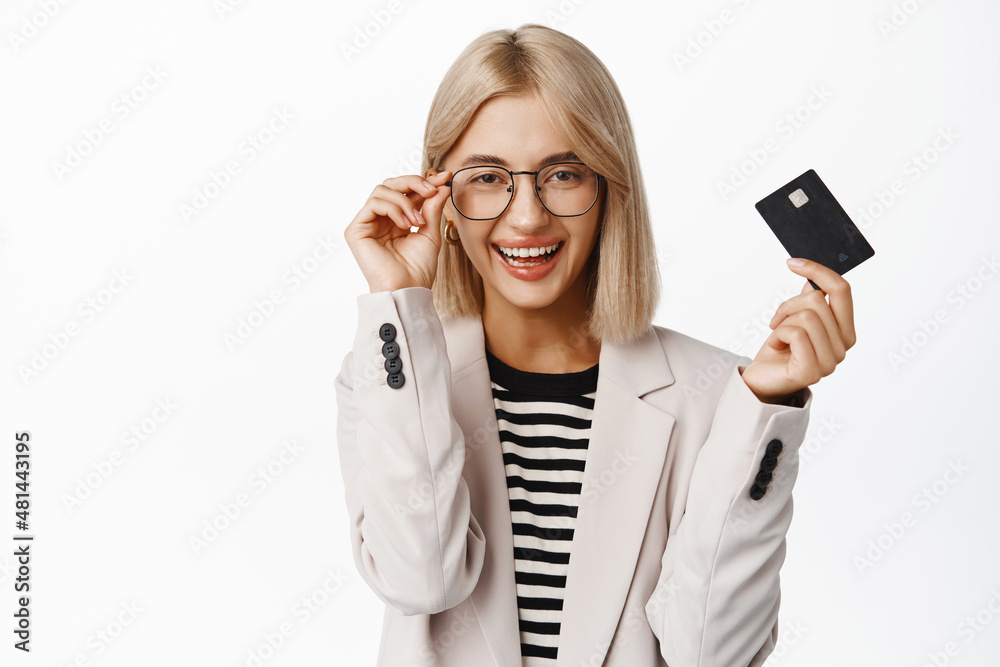 Image of corporate woman in glasses with credit card, buying contactless, making purchase and smiling, standing over white background Image of corporate woman in glasses with credit card, buying contactless, making purchase and smiling, standing over white background