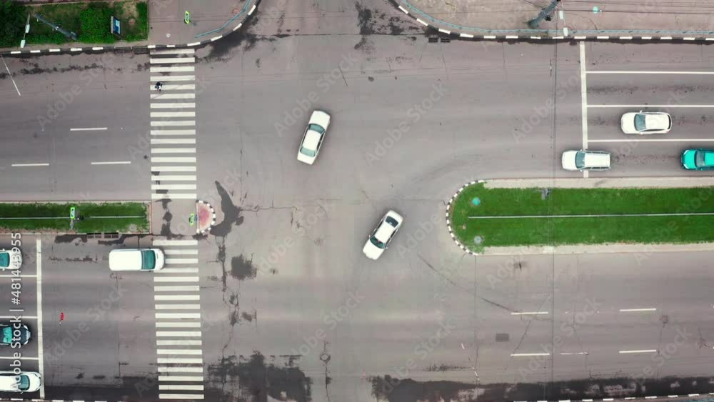 Car intersection: traffic in the city on a summer cloudy day. Cars pass the intersection of multi-lane road in the city. Road traffic at the city intersection - top view. Car intersection: traffic in the city on a summer cloudy day. Cars pass the intersection of multi-lane road in the city. Road traffic at the city intersection - top view.