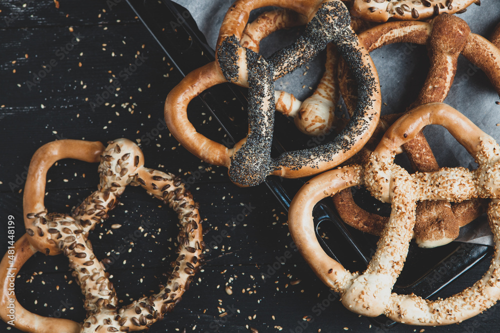 Fresh prepared homemade soft pretzels. Different types of baked pretzels with seeds on a black background