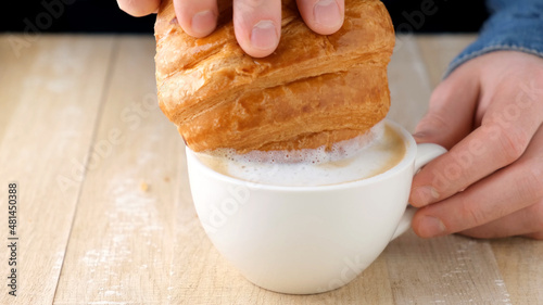 Dip croissant in coffee cappuccino. Breakfast or coffee break in cafe