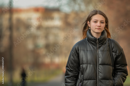 A young beautiful girl in a dark jacket is walking down the street.