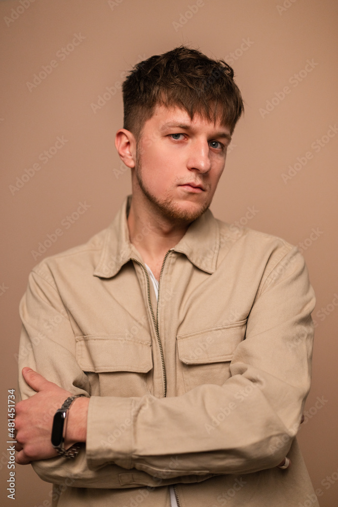Obraz premium Handsome man in fashionable outerwear with stylish beige jacket and white t-shirt posing on a beige background and looking at the camera