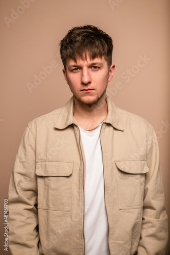 Beautiful young guy model with a fashionable hairstyle in a beige jacket and a white T-shirt in the studio, looking into the camera © alones