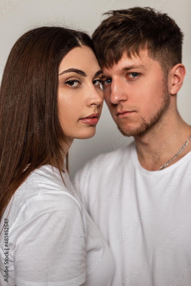 Beautiful young couple in stylish classic white t-shirts in the studio. Pretty woman and a handsome man with a haircut in fashionable clothes in the studio. Beautiful young couple in stylish classic white t-shirts in the studio. Pretty woman and a handsome man with a haircut in fashionable clothes in the studio.