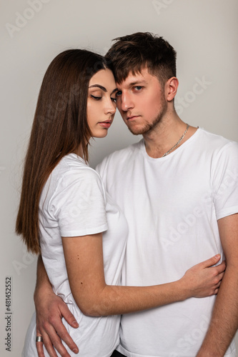 Beautiful young couple man and woman in white clothes in an embrace on a gray background in the studio. Love between a girl and a guy