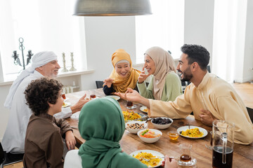 young arabian man talking to cheerful multicultural muslim family during dinner.