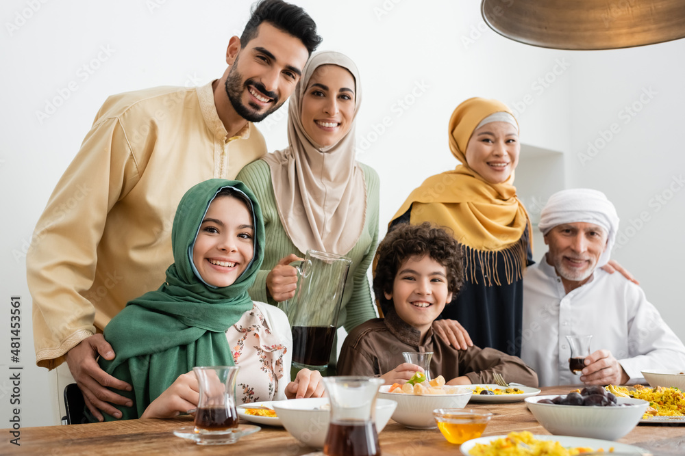 Fototapeta premium multicultural muslim family smiling at camera near served pilaf and tea.