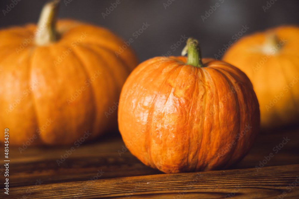 Three orange pumpkins on the brown table and grey background. Selective focus. Three orange pumpkins on the brown table and grey background. Selective focus.