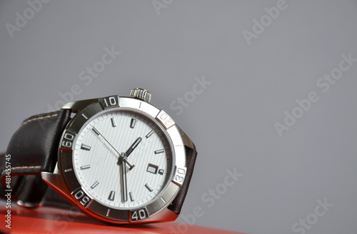 Wrist men's watch made of metal on a red table on a gray background.