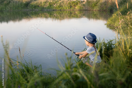 Little beautiful girl sits on the shore with a fishing rod and catches fish