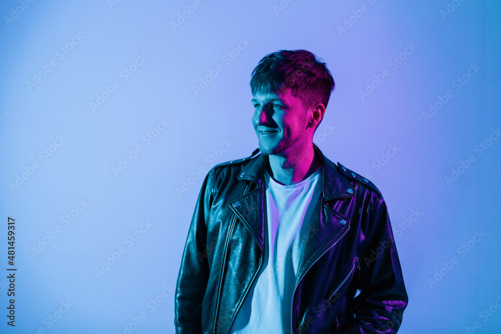Brutal handsome young man model with smile in black fashionable leather jacket on colorful pink neon lights Brutal handsome young man model with smile in black fashionable leather jacket on colorful pink neon lights