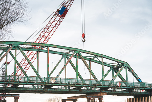 Workers cut an old steel bridge with a large crane on the water © blanke1973