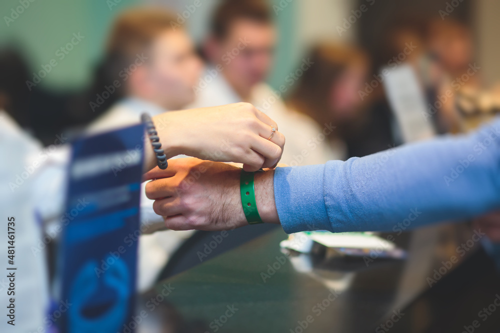 Obraz premium Process of checking in on a conference congress forum event, registration desk table, visitors and attendees receiving a name badge and entrance wristband bracelet and register electronic ticket,
