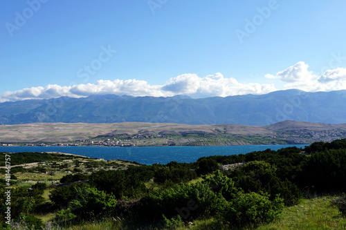 White clouds on the blue sky above green mountain and blue sea and green flora on the landscape in foreground © Happy window