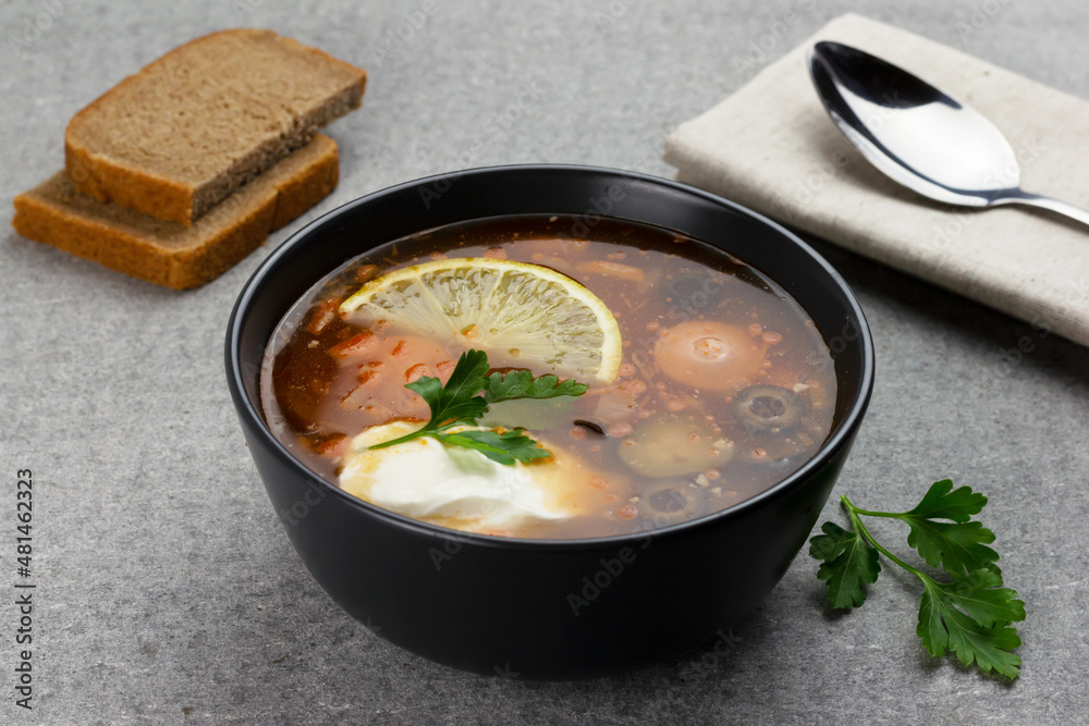 Traditional russian meat soup Solyanka in a black bowl and some bread