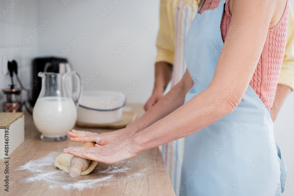 Cropped view of woman in apron rolling dough with pin near husband in kitchen. Cropped view of woman in apron rolling dough with pin near husband in kitchen.
