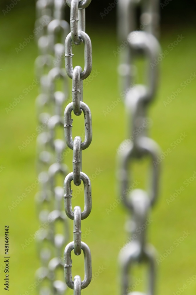 Iron chain extended vertically. Selective focus and green background. Iron chain extended vertically. Selective focus and green background.