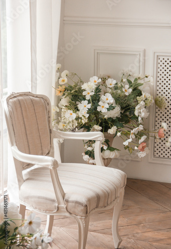 white armchair with spring flowers near the window in a classic interior near white wall background. free space