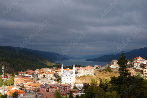 a small town Dospat Bulgaria with a mosque in sunlight against a stormy sky, mountains and a lake