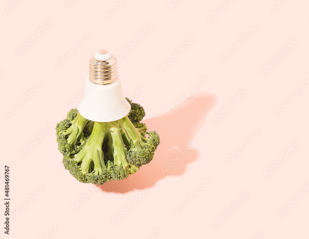Broccoli with light bulb cap on a light pink background. Surreal sustainable energy minimal concept.