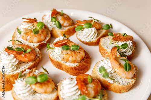 Small sandwiches with shrimps on a white plate.