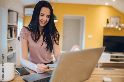 Middle aged woman using laptop and credit card while sitting at home kitchen Free Download Middle aged woman using laptop and credit card while sitting at home kitchen - GFXLoad