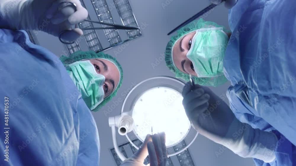 From below female surgeons in medical uniform using professional tools while standing under bright light in operating theater. High quality 4k footage