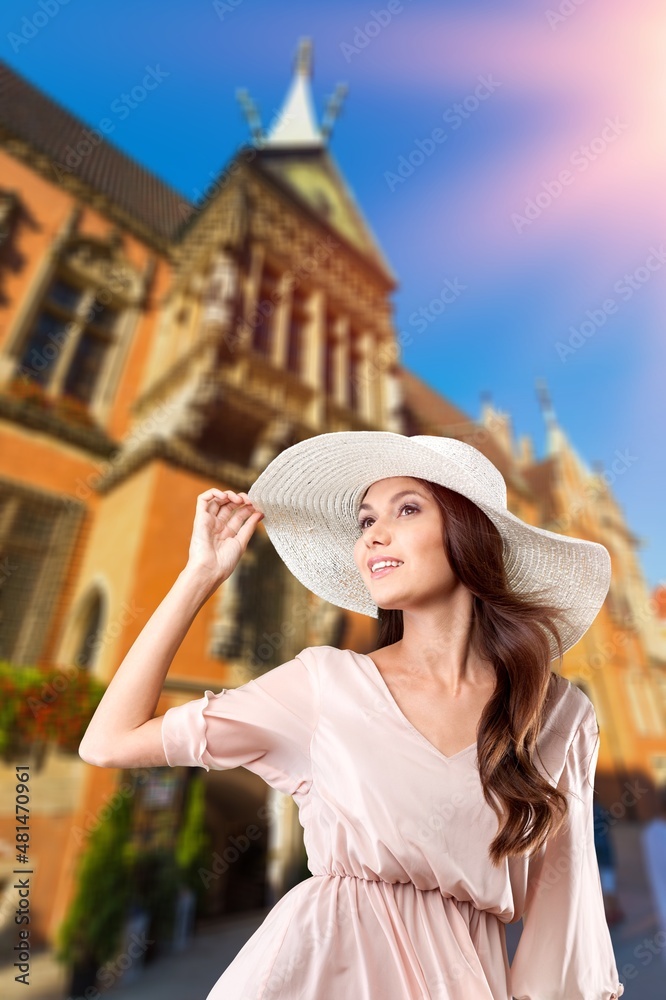 Happy young tourist woman in sun hat walking in city at sunset. A summer holiday vacation