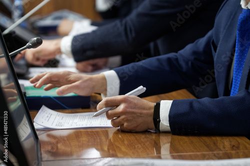 Hands of men - managers, officials, lawyers or businessmen sitting at table with microphones and monitors. Concept of negotiation, conference and teamwork. Reportage. Selective focus