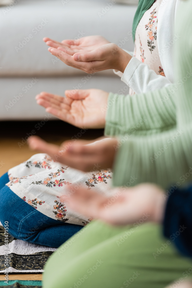 Fototapeta premium Cropped view of blurred arabian women and kid praying at home.