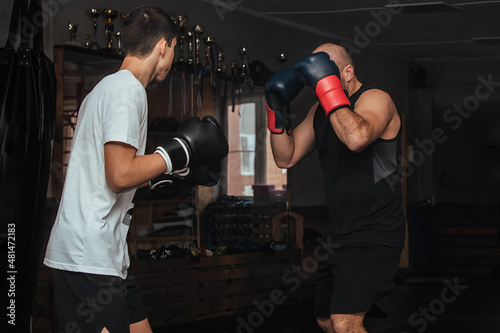 Two sportsmen boxers of different ages train in the classroom in the gym. They are practicing the Thai boxing technique in pairs