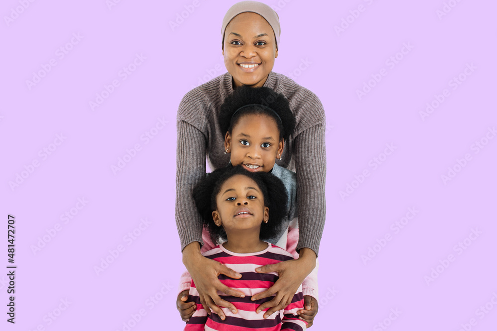 Charming african muslim woman in headscarf smiling on camera while embracing her two cute daughters. Isolated over purple studio background. Charming african muslim woman in headscarf smiling on camera while embracing her two cute daughters. Isolated over purple studio background.