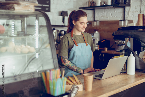 Young woman barista using laptop in coffee shop