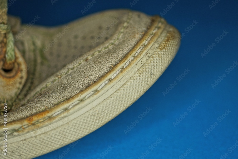 a part of a gray old shoe made of fabric with a leather sole stitched with thread stands on a blue table a part of a gray old shoe made of fabric with a leather sole stitched with thread stands on a blue table