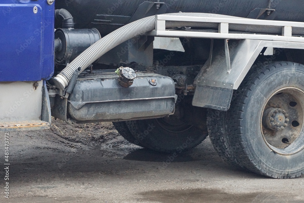 part of a truck with an iron gas tank and a black wheel on the street on a gray road