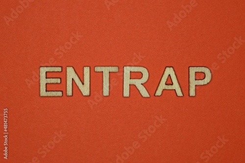 text the word entrap from gray wooden small letters on an red table