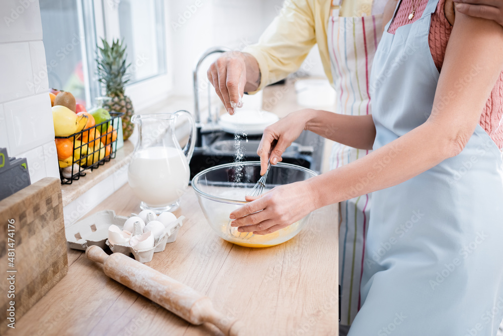 Cropped view of man pouring flour in bowl while wife mixing eggs in kitchen. Cropped view of man pouring flour in bowl while wife mixing eggs in kitchen.