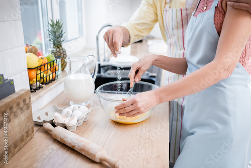 Cropped view of man pouring flour in bowl while wife mixing eggs in kitchen.
