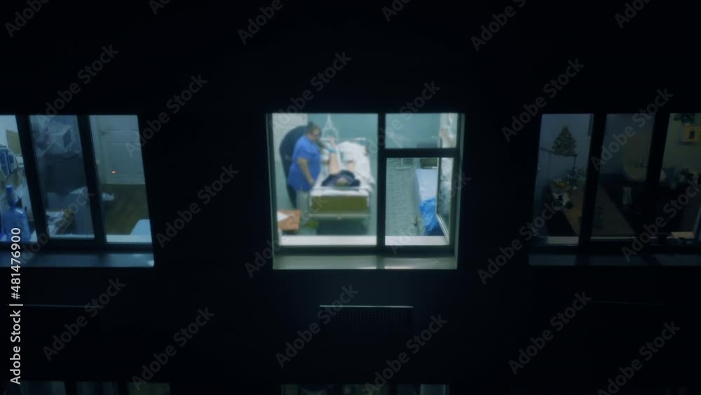 Operating room in a hospital with a surgeon and a nurse examining a patient before surgery. Aerial view outside through the window at night. Operating room in a hospital with a surgeon and a nurse examining a patient before surgery. Aerial view outside through the window at night.