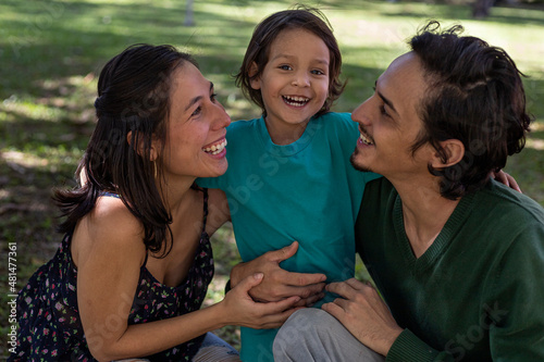 Young Latino parents happily share with their 3 year old son at the park. Family concept.