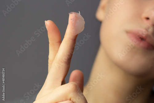 A young woman is applying petroleum jelly to her face. Concept of slugging. photo