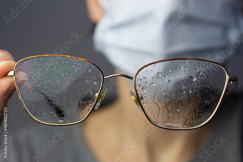 A woman in protective face mask is spraying her glasses with an anti-fog spray.