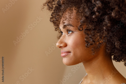 Charming multiracial woman posing against beige wall