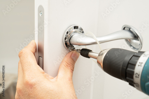 Service man installing magnetic lock and a door handle on an interior door using a screwdriver.