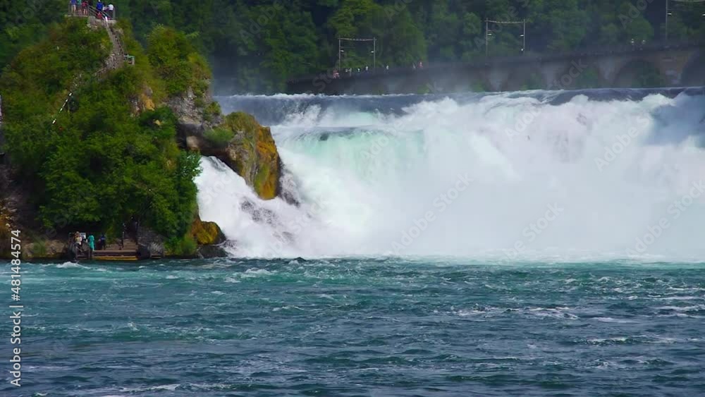 The churning Rhine roars its way down stream as tourists walk up and down the middle cliff, Rhine Falls, Neuhausen near Schaffhausen, Switzerland. The churning Rhine roars its way down stream as tourists walk up and down the middle cliff, Rhine Falls, Neuhausen near Schaffhausen, Switzerland.