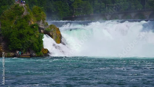 The churning Rhine roars its way down stream as tourists walk up and down the middle cliff, Rhine Falls, Neuhausen near Schaffhausen, Switzerland.
