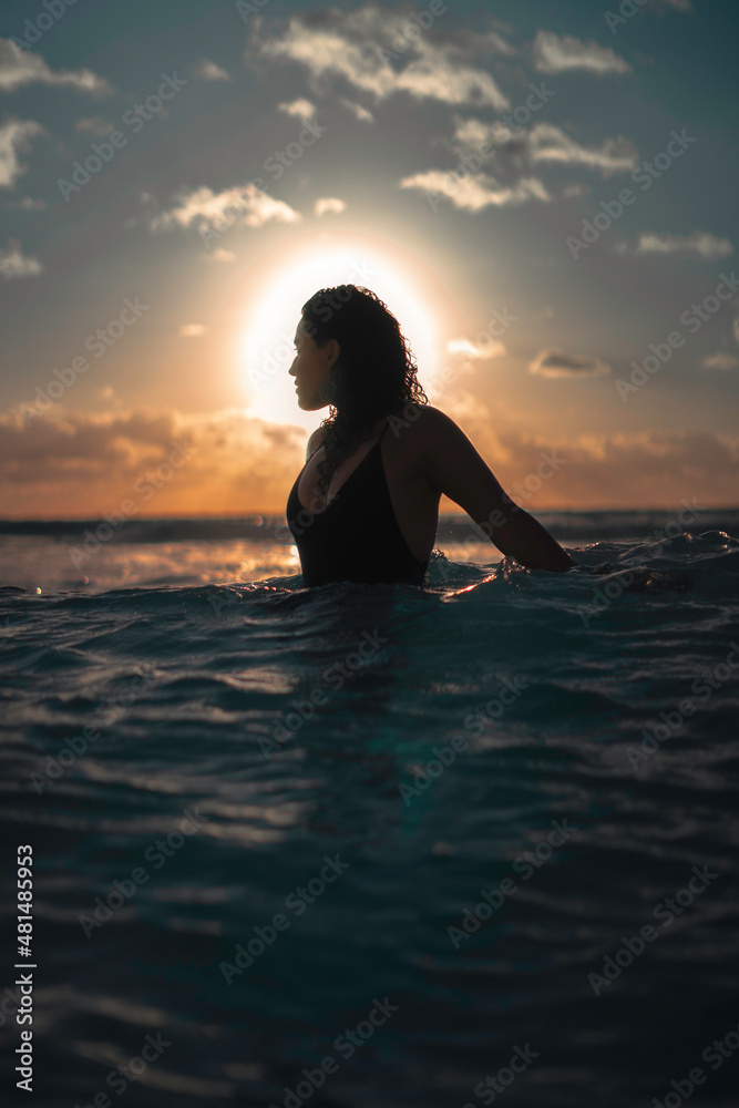 Silueta de una hermosa mujer joven, latina nadando y disfrutando de la vista, en el mar al amanecer, a contraluz