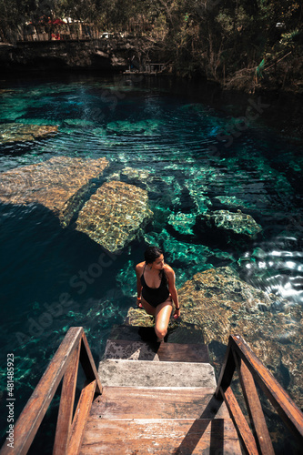 Mujer joven, atractiva, latina en bikini, parada en la escalera de un cenote cristalino, cerca de Tulum México